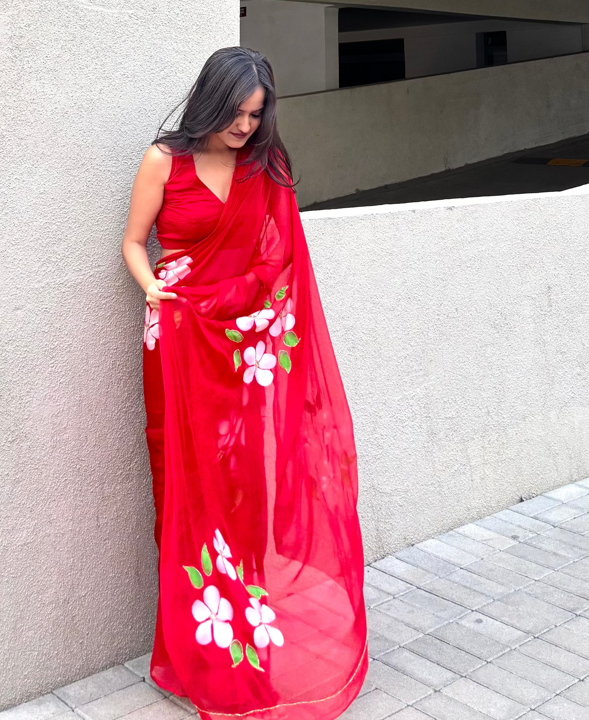 Woman wearing a red saree with floral patterns against a concrete wall.